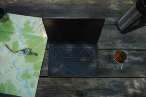 Outdoor Workstation Setup with a Laptop, Map, Compass, and Tea photo