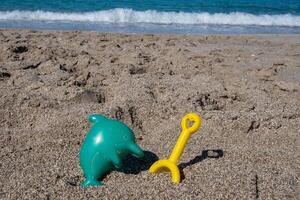 Beach toys dolphin and rake waiting for children playing on sand photo