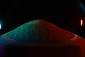 Rainbow sparkly hourglass sand on dark background. Minimalist low key poto for concepts of time, travel to the desert photo