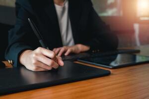 A person in a suit using a digital tablet and stylus at a wooden desk, highlighting modern technology in a professional environment. photo