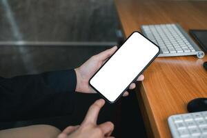 Professional holding a smartphone with a blank screen at a wooden office desk, ideal for app or website mockup. photo