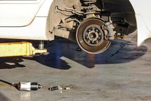 The vehicle lifted from the hydraulic lift shows brake discs and suspension, the rear wheels have been removed for maintenance, and tools are placed on the ground nearby. photo