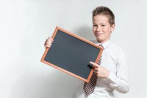 Smiling schoolboy pointing on clean black chalkboard photo