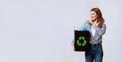 Waste Recycling Concept. Millennial Lady Carrying Black Container With Empty Plastic Bottles, Young Eco-Activist Woman Sorting Garbage For Recycle, Standing Over Grey Studio Background, Free Space photo