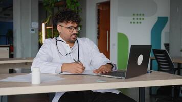 Doctor having call and taking notes on laptop video