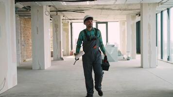 Construction worker walking in unfinished building carrying paint roller and toolbox video