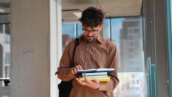 University student reading book and holding other books in corridor video