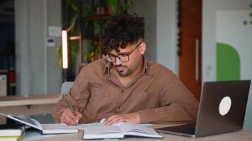Focused student taking notes while studying on laptop video