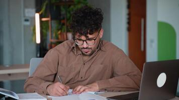 Focused employee working on laptop and taking notes in modern office video