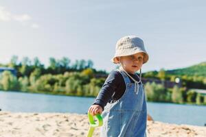 A Cherubic Toddler Enjoys a Beautiful Beach Day with a Brightly Colored Toy Shovel, Filled with Sunshine, Joy, Adventure, and Discovery with Family and Friends at the Tranquil Waterfront photo