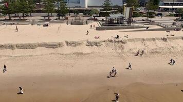 Aerial footage captures people walking along Broadbeach, Gold Coast, under sunny skies, highlighting coastal erosion and urban backdrop video
