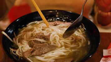 A person savors a bowl of Vietnamese pho with chopsticks and spoon in a cozy setting video