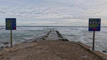 Waves hitting rock pools with warning signs visible video