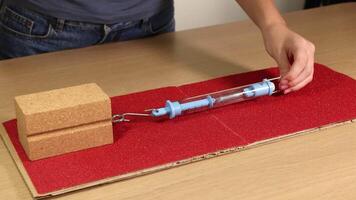 A wooden block is dragged across sandpaper using a spring scale, illustrating friction and force measurement video