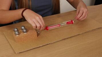 A person uses a spring scale to measure force needed to drag weights on cardboard, illustrating friction principles video