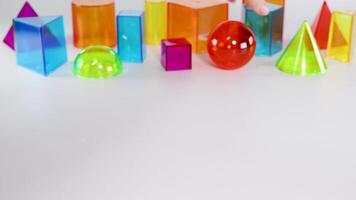 Hands interact with vibrant 3D geometric shapes on a white surface, illustrating basic mathematical concepts in a playful setting video