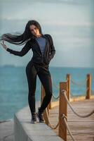Woman posing confidently on a waterfront walkway during golden hour with flowing hair in a casual outfit photo