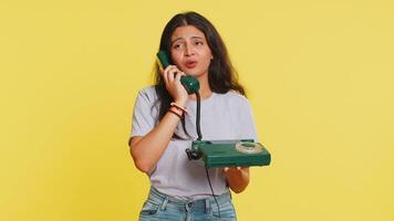 Tired bored Indian woman talking on wired vintage telephone of 80s, fooling, making silly faces, exhausted of tedious story, not interested in communication talk. Arabian girl on yellow background video