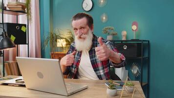 Like. Smiling Caucasian senior man looking approvingly at camera showing double thumbs up sign positive something good great news positive feedback. Happy grandpa with laptop at home office table. video