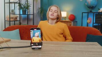 Caucasian teenager boy filming recording trendy selfie on smartphone at home. Demonstrating dance moves, sitting on couch by table, creating content for social media with enthusiasm creativity video