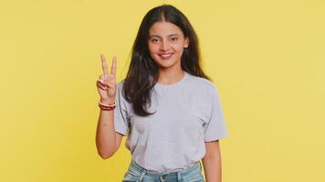 Happy Indian young woman showing victory sign, hoping for success and win, doing peace gesture, smiling with kind optimistic expression, celebrate. Arabian girl isolated on studio yellow background video
