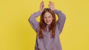 I am little bunny rabbit. Lovely funny young preteen child girl kid smiling friendly and doing bunny ears gesture on head, having fun, fooling with humorous comical mood. Children on yellow background video