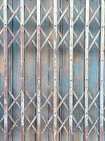 Rusty metal gate with crisscross pattern and peeling paint old and weathered surface blue and brown tones vertical and diagonal lines industrial style textured background vintage appearance photo