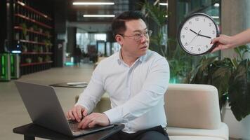kinesisk affärsman arbetssätt på bärbar dator med ångest kontroll tid på klocka, löpning sent till arbete varelse i fördröjning deadline. chef man i skjorta ser på timme, minuter oroande till vara punktlig i lobby. video