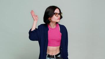 Young woman playfully imitates knocking motion, leans forward smiling humorously while asking who is there. Girl clearly demonstrates playful and engaging humorous interaction, on gray background video