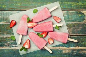 Homemade strawberry ice cream or popsicles on rustic wooden table, frozen fruit juice, top view photo