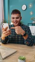 Smiling happy man using smartphone application online pointing showing like thumbs up remote distance job working from home office. Guy freelancer recommends to use a good mobile program. Vertical video