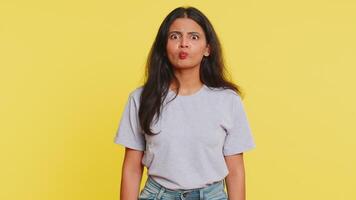 Surprised funny comical playful Indian woman making fish grimace pout lips, smooching choking and looking with shocked dumb idiotic expression doing duck face fooling around. Girl on yellow background video