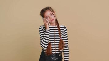 Disinterested preteen child girl kid having annoyed boring talk on smartphone. Children tired sleepy freelancer talking on mobile phone with friend, making online conversation on beige background video