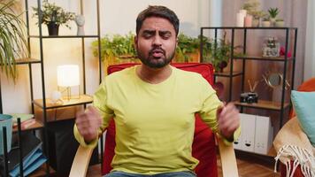 What. Why. Frustrated Indian man raising hands in indignant expression, asking reason of failure, demonstrating disbelief irritation by troubles, quarrel at home room apartment. Guy sits on chair video