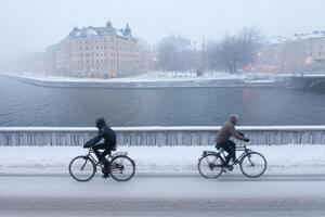 Winter Cycling in Stockholm A Scenic Ride Through Snowy Cityscapes. Witness the beauty of a snow covered bridge, river, and charmi photo