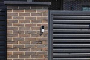 A sleek intercom device is installed on a stylish brick wall, facilitating secure communication at the entrance of a contemporary property photo