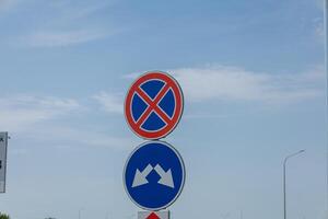 A no parking sign and a directional arrow are positioned along a road under a clear blue sky with minimal clouds photo