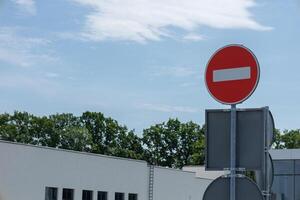 A bright red do not enter sign stands prominently in front of modern buildings under a blue sky, conveying a clear road instruction photo