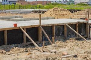Workers are preparing a concrete foundation for a new residential building, with wooden supports installed and sandy terrain surrounding the area photo