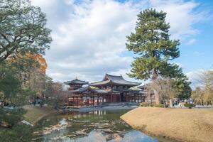 Byodo-in Temple Uji Kyoto Japan, Traditional architecture beside a serene pond under a cloudy sky. photo