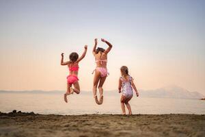 Joyful sisters jumping on the beach at sunset by the water photo