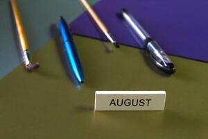 On a dark multi-colored background lie stationery, in the foreground is the word August. photo