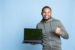 Young friendly african american guy feeling positive next to copy space mockup, gesturing for an advertisement against blue background. Male model with a hoodie smiling in studio. photo