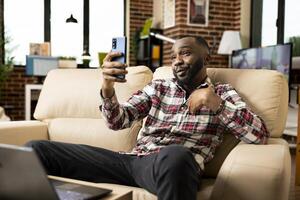 Self employed bearded man in call with family during break from remote work responsibilities. Black entrepreneur negotiating business details while working from home using smartphone. photo