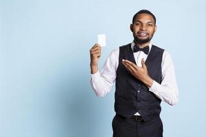 Classy hotel bellboy in tuxedo giving the room access key card to guest after check in, offering excellent concierge services at holiday resort. Employee working in hospitality industry. photo