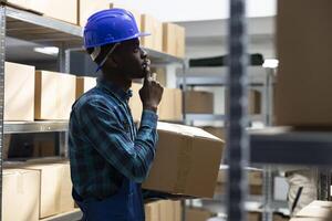 Black worker manages business logistics to ensure operational control of the merchandise inventory system. Shelving units in a warehouse lined with packages and boxes, storage process. photo