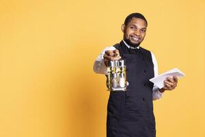 Restaurant employee with apron and cruet set takes orders from clients, writing down meal information on a notebook for customer satisfaction. Caterer butler in service oriented industry. photo