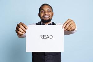 African american hotel personnel getting the attention of clients with an important message, asking them to read the note on the paper sign. Bellboy with professionalism working in tourism. photo