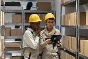 Multiethnic staff scanning goods on warehouse shelving unit to manage inventory and stock delivery. Control systems and logistics processes ensure smooth operation within the industrial depot. photo