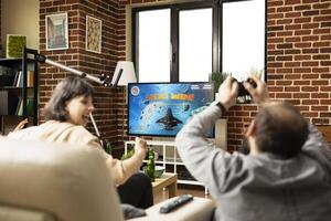 White man and woman relax together, celebrating shared game victory. Young caucsasian adults with raised hands, cheering and enjoying drinks on sofa while TV flashes winning message. photo